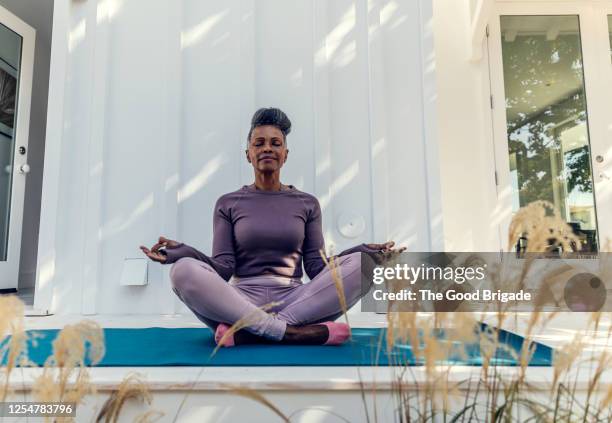 mature woman meditating in backyard - lotuspositie stockfoto's en -beelden