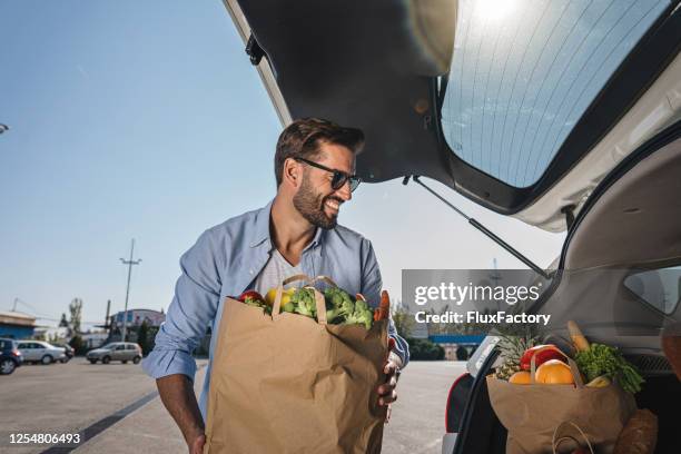 papá poniendo una bolsa de verduras en el maletero de su coche - parking meter fotografías e imágenes de stock