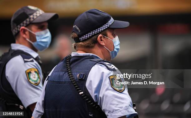 Police officers wear face masks as they watch passengers arrive from a Qantas flight at Sydney Airport on one of the last flights out of Melbourne to...