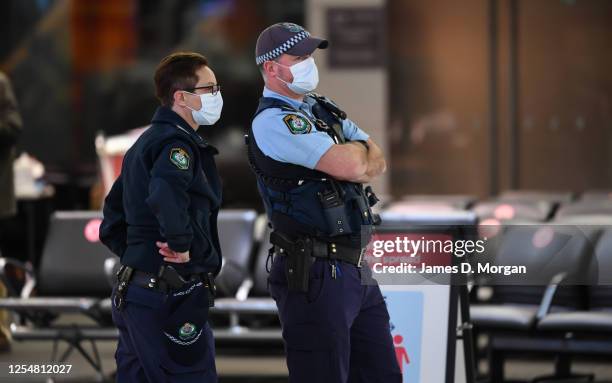 Police officers wear face masks as they watch passengers arrive from a Qantas flight at Sydney Airport on one of the last flights out of Melbourne to...