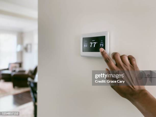 woman adjusts thermostat - thermostat fotografías e imágenes de stock