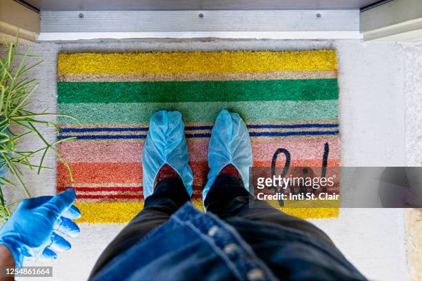 man with shoe protectors and gloves standing on door mat in at home doorway - shoe covers stock pictures, royalty-free photos & images