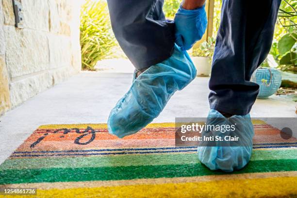 man standing on doormat putting on shoe protector - shoe covers stock pictures, royalty-free photos & images