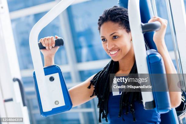 zwarte jonge vrouw bij de gymnastiek die haar wapens op machine uitwerkt - bicep curl stockfoto's en -beelden