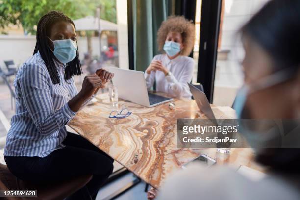 Drei Geschäftsfrauen bei einem Treffen in einem Café, während sie während einer Pandemie Schutzmasken tragen
