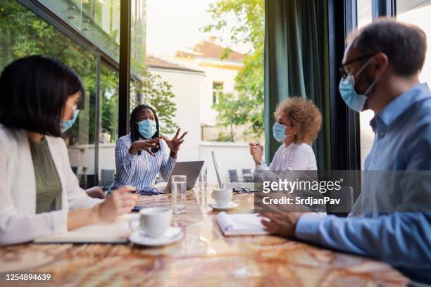 diverse group of business people having a meeting at the coffee shop while wearing protective masks during coronavirus pandemic - social distancing meeting stock pictures, royalty-free photos & images