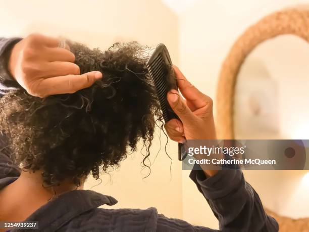 mid adult african-american woman detangles wet natural hair with comb - kinky stock-fotos und bilder