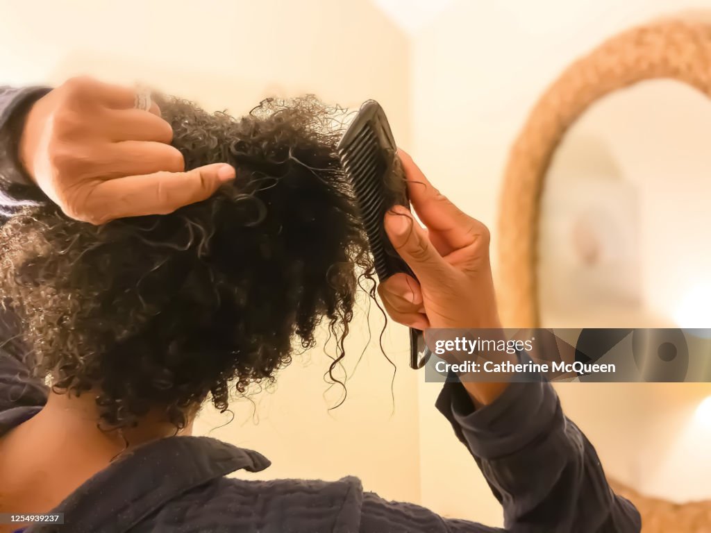 Mid adult african-american woman detangles wet natural hair with comb