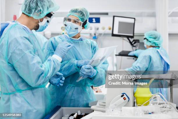 mannelijke en vrouwelijke artsen die in icu bespreken - face mask protective workwear stockfoto's en -beelden