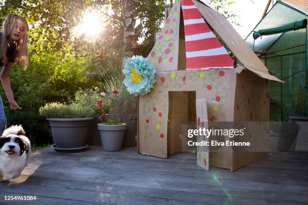 teenage girl chasing rebellious puppy next to a homemade playhouse made from recycled cardboard boxes - playhouse stock-fotos und bilder