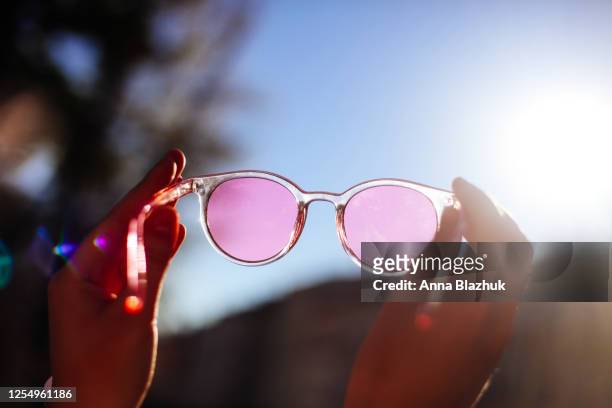 street summer picture of woman holding pink sunglasses against blue sky and sun. positive emotions concept. summer fashion, lifestyles concept. - pink hat - fotografias e filmes do acervo