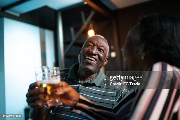 senior-paar toastet bier in einer bar - old couple restaurant stock-fotos und bilder