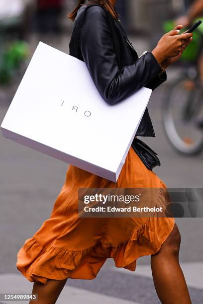 Passerby wears a black leather jacket, an orange flowing ruffled skirt, an Iro white paper shopping bag, on July 04, 2020 in Paris, France.