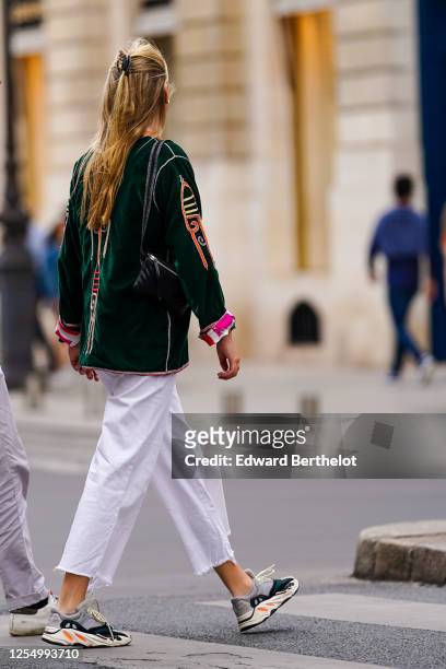 Passerby wears white ripped denim cropped jeans, sneakers shoes, a green velvet jacket with printed geometric patterns and pink cuffs, a black...