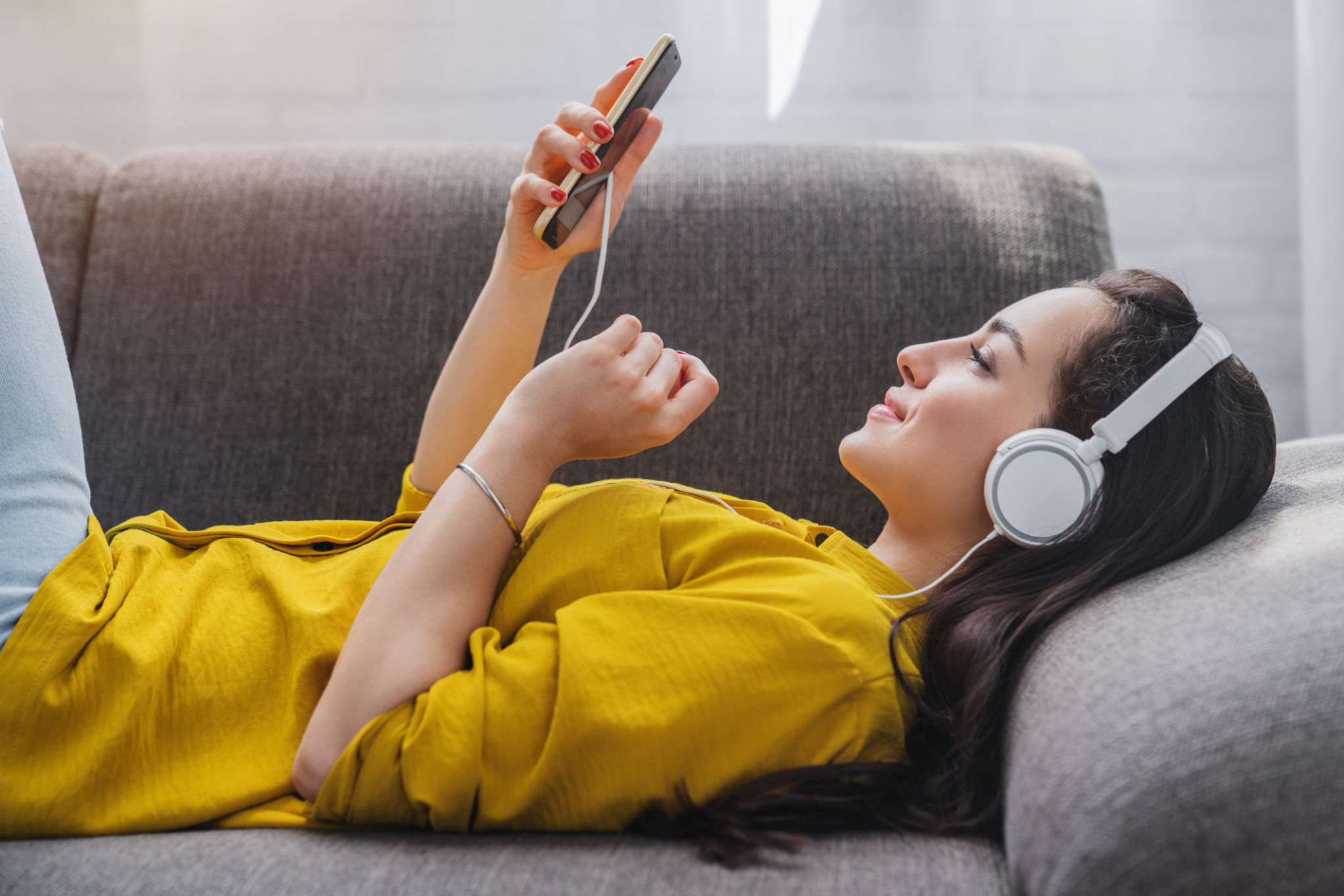 Side view of young woman listening to music online on smartphone in headphones Side view of young woman listening to music online on smartphone in headphones