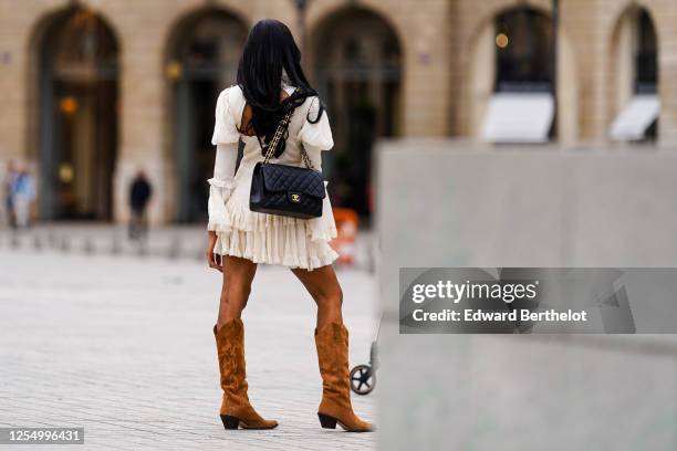 Passerby wears a white ruffled lace pleated dress, a black leather quilted Chanel bag, brown suede high cow-boy pointy boots, on July 04, 2020 in...