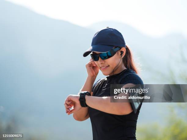 female runner standing outside and looking at watch - boné de basebol imagens e fotografias de stock
