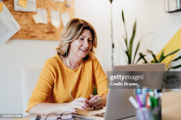 mature businesswoman working from home and attending video conference meeting - yellow business stock pictures, royalty-free photos & images