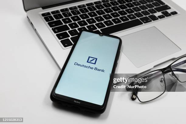 In this photo illustration a Deutsche Bank logo is displayed on a smartphone screen above a Macbook next to glasses in Athens, Greece on May 15, 2023.