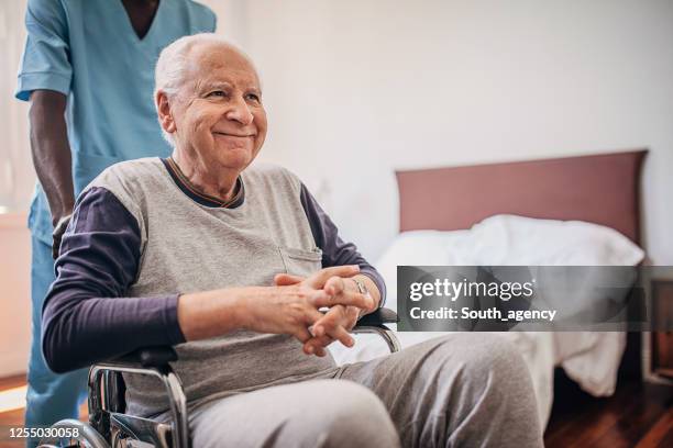 enfermera masculina empujando a la tercera edad en silla de ruedas en el hogar de ancianos - geriatria fotografías e imágenes de stock