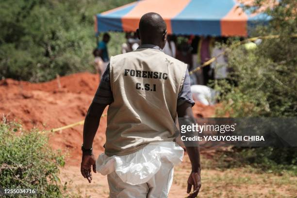 An officer of the Directorate of Criminal Investigations walks at the mass-grave site in Shakahola, outside the coastal town of Malindi, on April 25,...