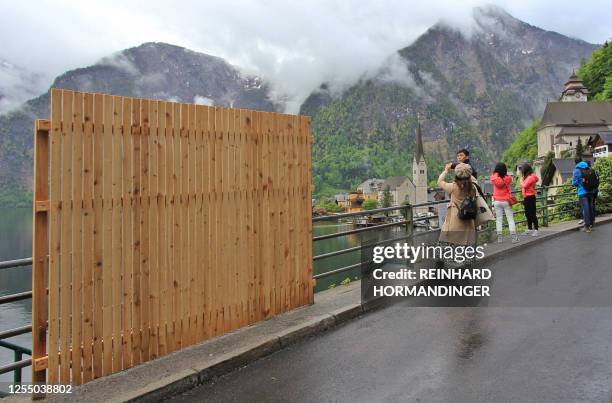 Provisional wooden fence is partially blocking the beautiful view, as visitors take selfies with the landscape, in the tourist community of Hallstatt...