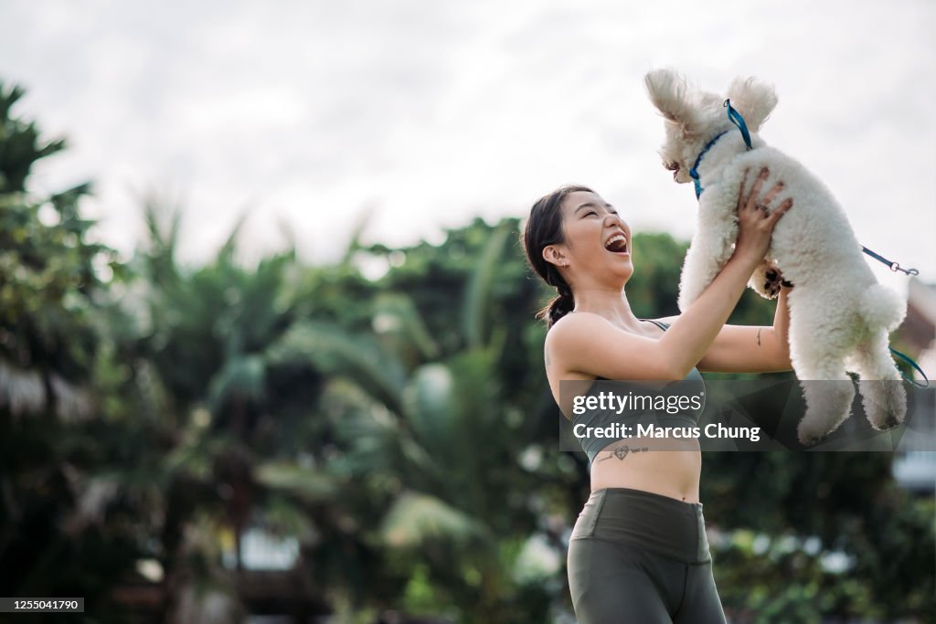 Asiatica cinese sorridente femmina che gioca con il suo baroniere giocattolo animale domestico al parco pubblico