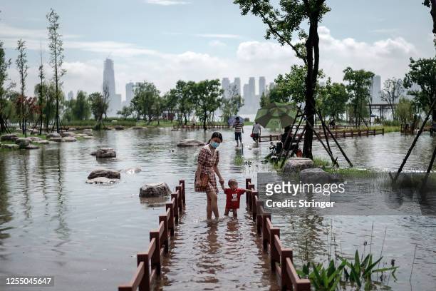 Woman with her child wear a mask while walking through the flooded Jiangtan park damaged by heavy rains along the Yangtze river on July 8th, 2020 in...