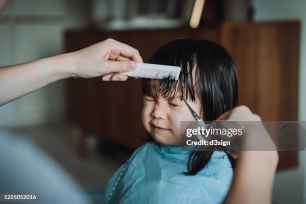 cropped hands of young asian mother cutting hair of her little daughter at home - hairdresser ストックフォトと画像