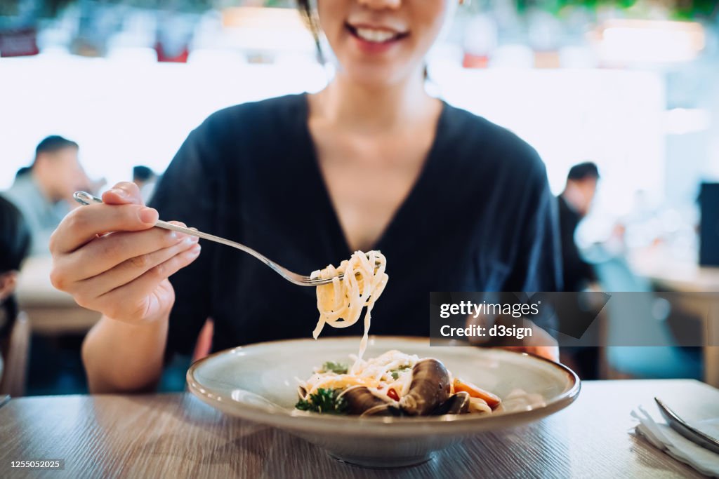 Young Asian woman eating freshly served seafood pasta for lunch in a restaurant