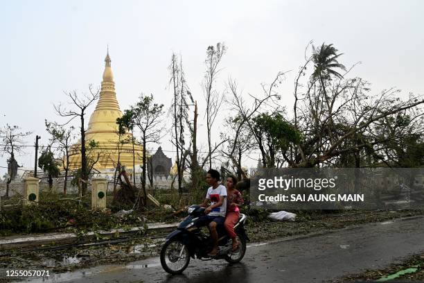People ride a motorcycle past broken trees next to a temple in Sittwe, in Myanmar's Rakhine state, on May 15 after cyclone Mocha made a landfall....