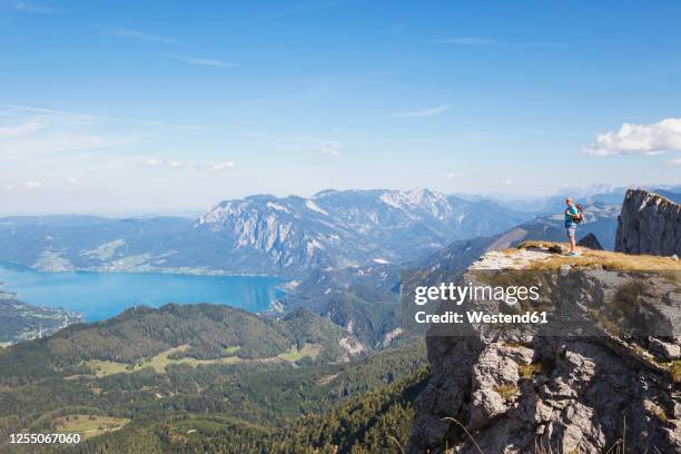 full length of hiker standing on spinnerin peak while looking at attersee against blue sky - attersee stock pictures, royalty-free photos & images