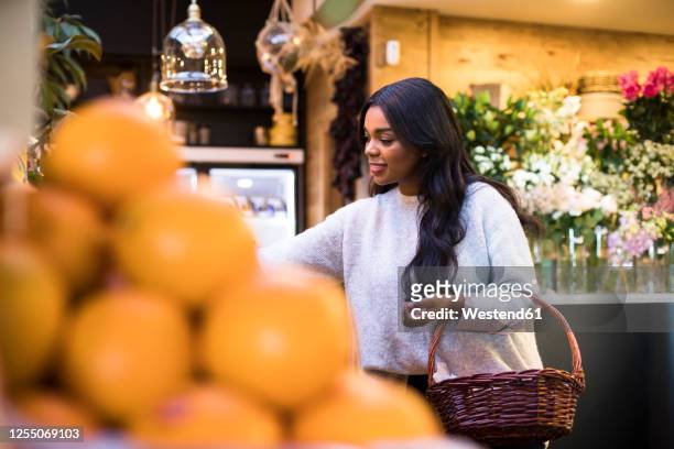 young woman carrying wicker basket while shopping in grocery store - oranges in basket at food market stock pictures, royalty-free photos & images