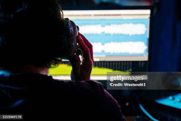 man holding headphones while using computer in recording studio at home - geluidsoverlast stockfoto's en -beelden
