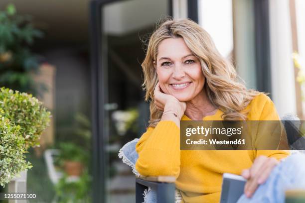 portrait of happy mature woman sitting on terrace with digital tablet - blonde frau stock-fotos und bilder