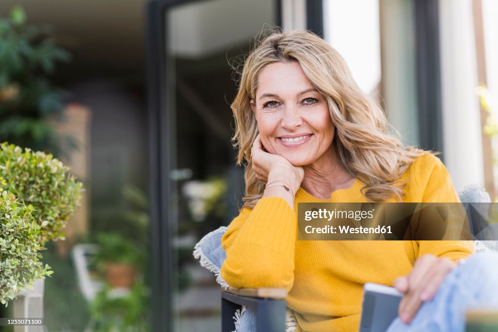 Portrait of happy mature woman sitting on terrace with digital tablet