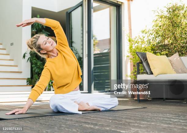 mature woman doing yoga exercise on terrace - donne bionde scalze foto e immagini stock