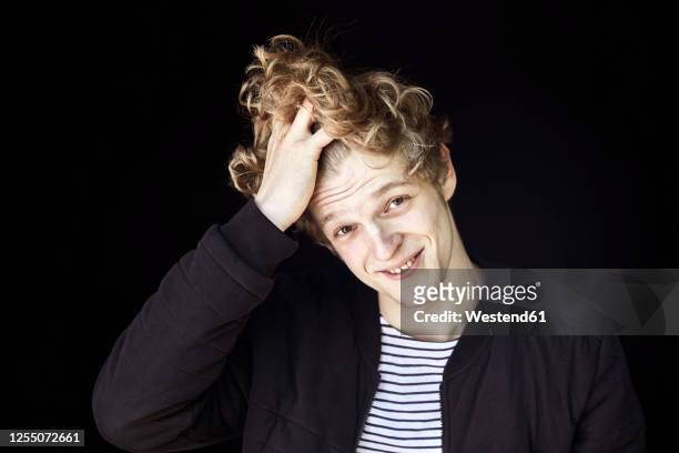 portrait of smiling young man with hand in hair against black background - tousled hair man stock pictures, royalty-free photos & images