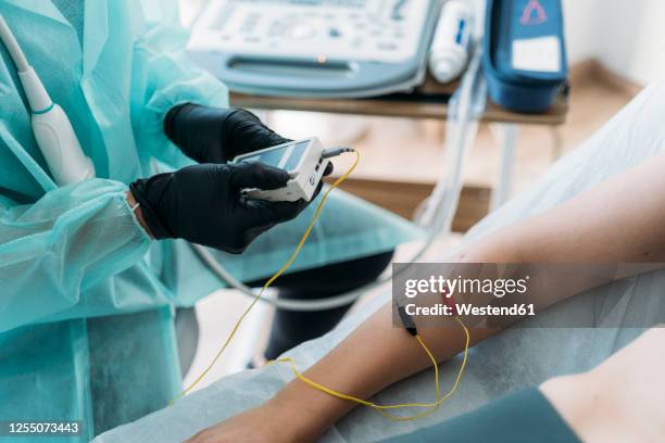 doctor wearing protective clothes examining woman's arm with electrodes - electrode stock pictures, royalty-free photos & images