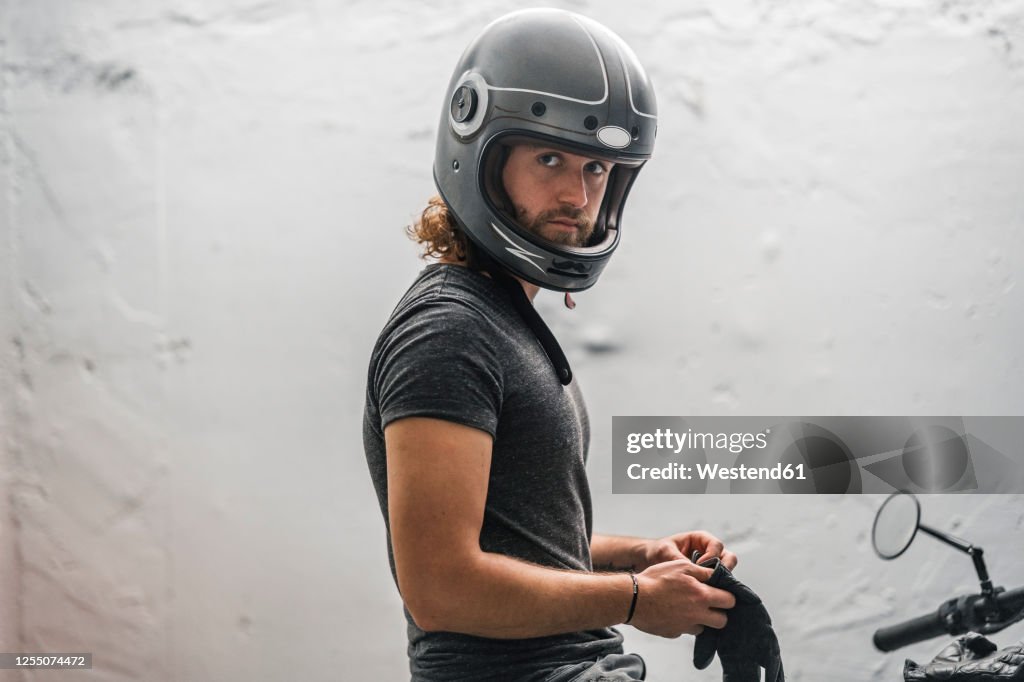 Young man putting on his gloves sitting on motorcycle