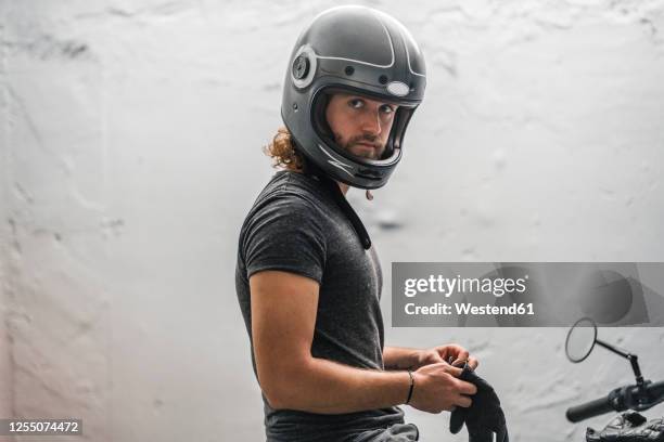 young man putting on his gloves sitting on motorcycle - biker foto e immagini stock