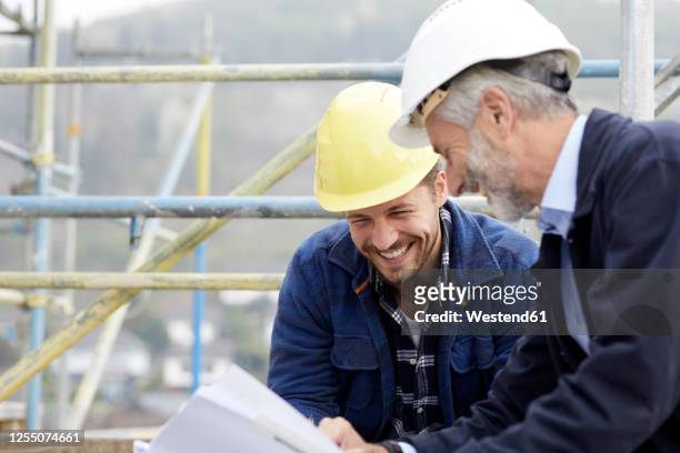 happy architect and worker discussing building plan on scaffolding on a construction site - architect industrie stock-fotos und bilder