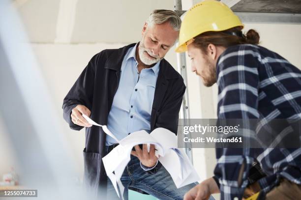 architect and worker discussing building plan on a construction site - architect construction stock pictures, royalty-free photos & images