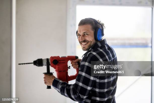 portrait of smiling worker using electric drill on a construction site - loud man imagens e fotografias de stock