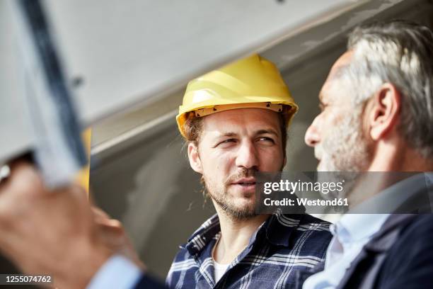 architect and worker talking at the window on a construction site - vorarbeiter stock-fotos und bilder