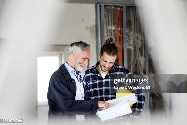 architect explaining building plan to worker on a construction site - construction meeting helmet stock pictures, royalty-free photos & images