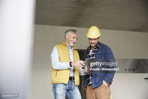 architect and worker sharing tablet on a construction site - vakmanschap bouw stockfoto's en -beelden