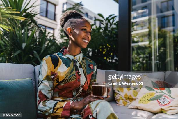 portrait of happy young woman sitting on couch in garden drinking black coffee - coffee happy stockfoto's en -beelden