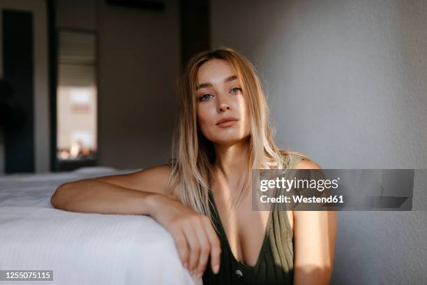 seductive young woman sitting by bed in bedroom at home - frau brust erotisch stock-fotos und bilder