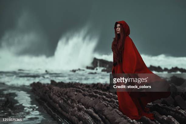 mysterious woman wearing red on the coastline - red dress stock pictures, royalty-free photos & images